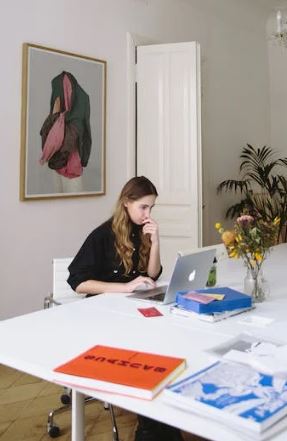 A woman sat a white desk in front of an open laptop.