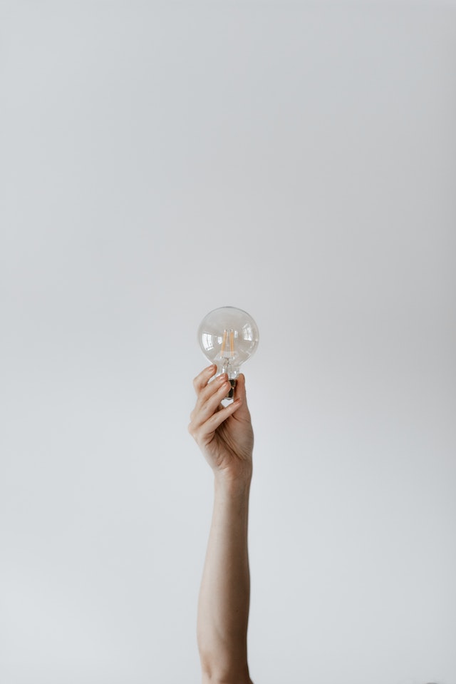 A woman's outstretched arm holding a lightbulb in the air.