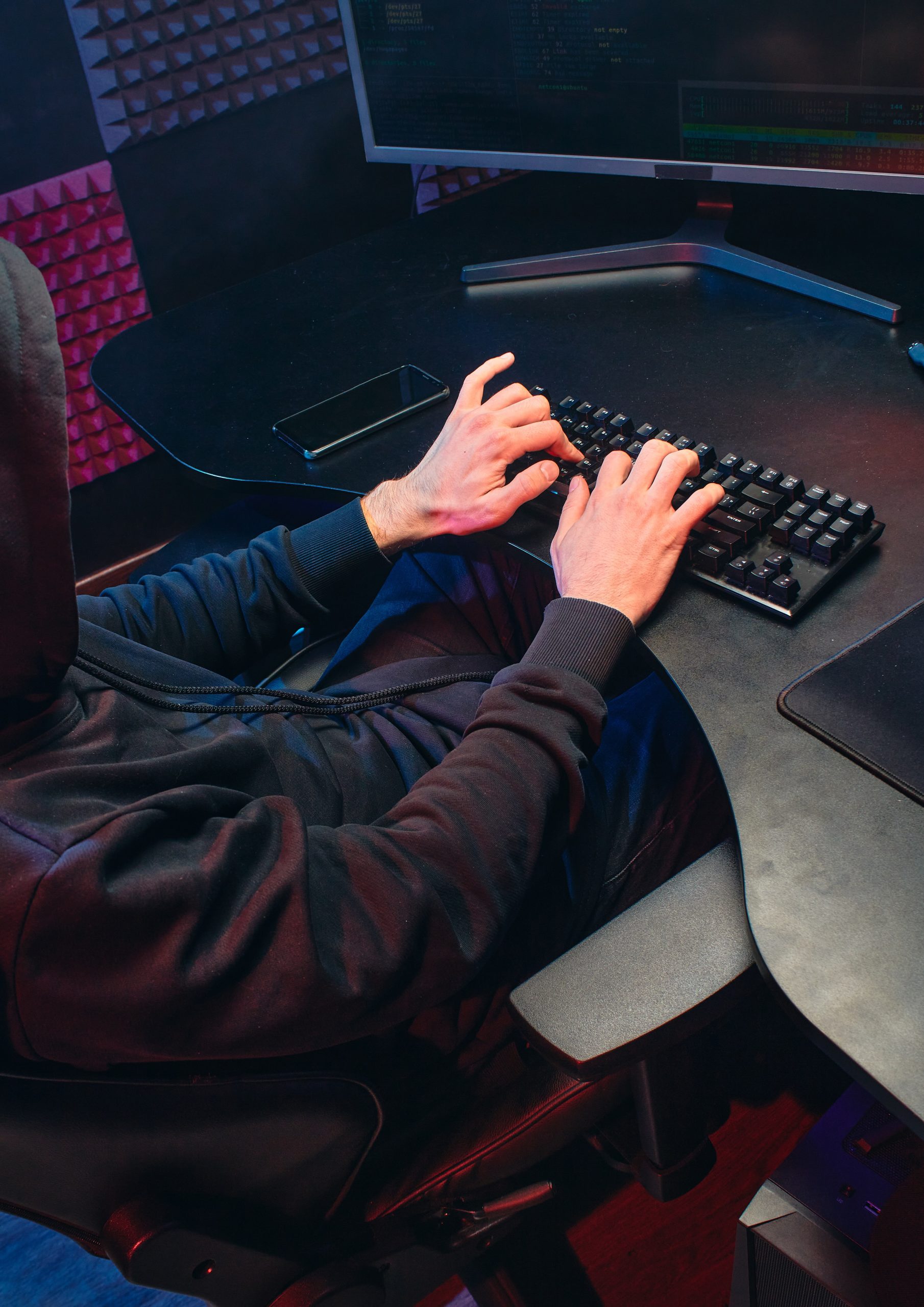 A hooded individual sat at a desk typing on a keyboard